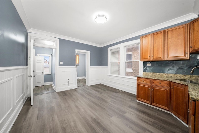 kitchen with light stone counters, brown cabinets, dark wood-style flooring, ornamental molding, and a sink