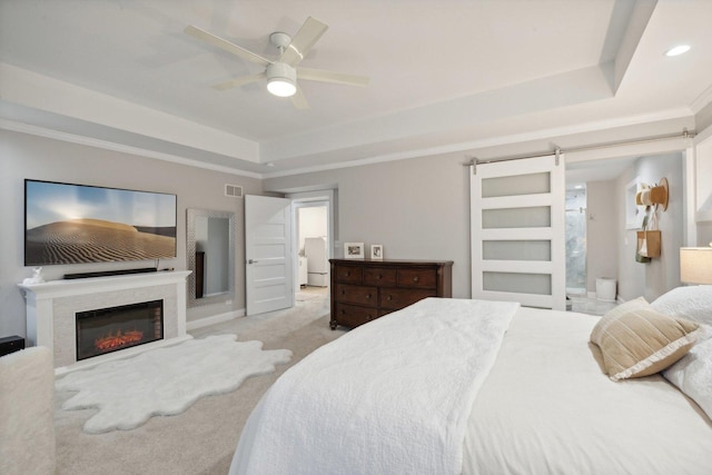 carpeted bedroom featuring a barn door, ceiling fan, ornamental molding, and a tray ceiling