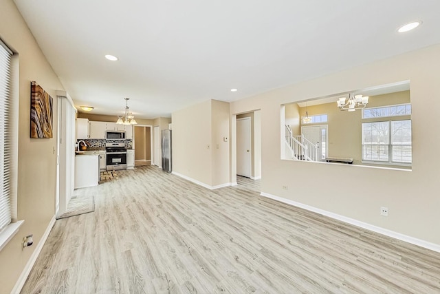 unfurnished living room with recessed lighting, a notable chandelier, baseboards, light wood-style floors, and stairs