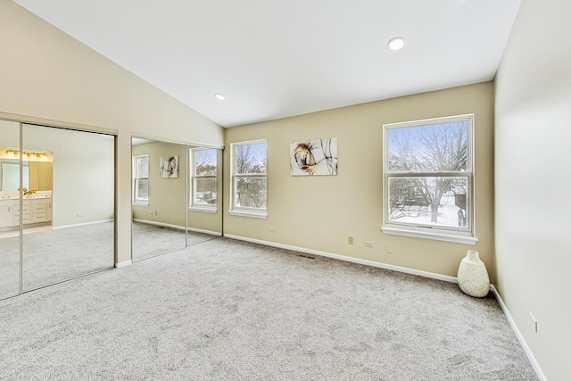 unfurnished bedroom featuring lofted ceiling, carpet floors, baseboards, and multiple closets