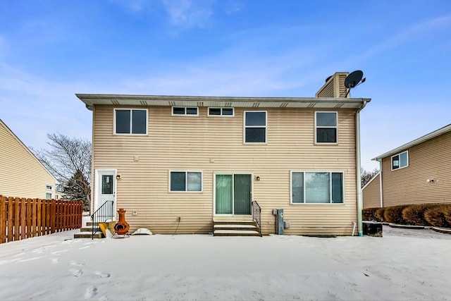 snow covered back of property with entry steps, a chimney, and fence