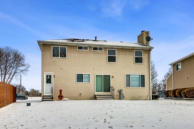 back of house featuring entry steps, a chimney, and fence