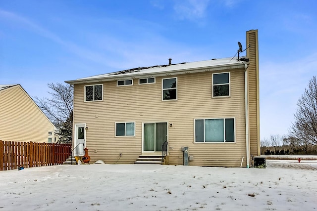 snow covered property with entry steps, fence, and a chimney