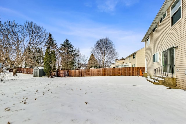 yard covered in snow with entry steps, a fenced backyard, an outdoor structure, and a storage shed