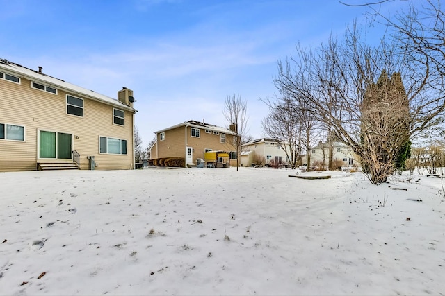 snow covered rear of property with entry steps, a chimney, and a residential view