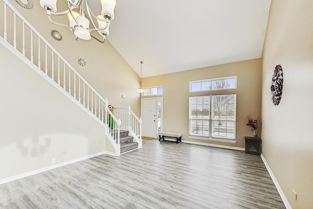 entryway featuring a chandelier, high vaulted ceiling, wood finished floors, baseboards, and stairway