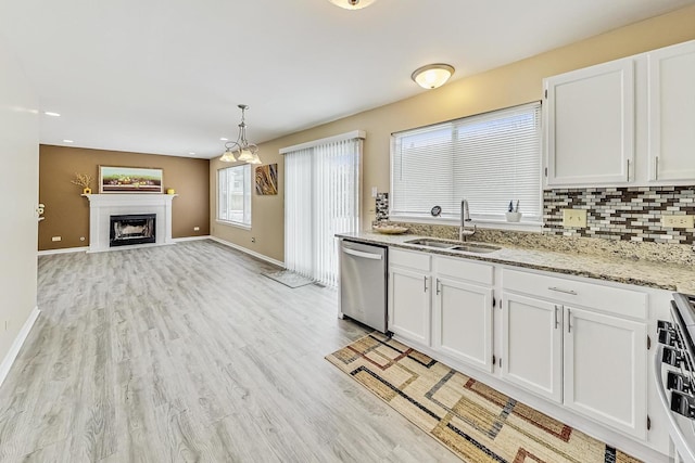 kitchen featuring tasteful backsplash, stainless steel dishwasher, a fireplace with flush hearth, white cabinetry, and a sink