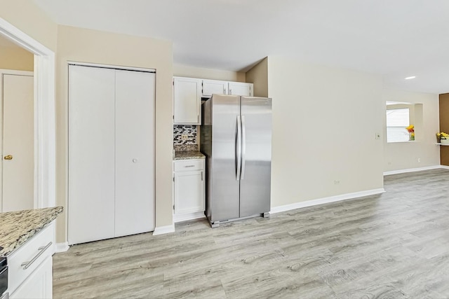 kitchen with light wood finished floors, backsplash, freestanding refrigerator, white cabinets, and light stone countertops