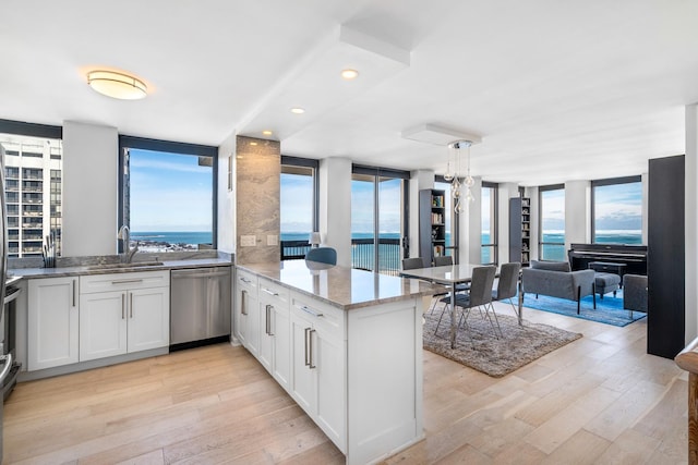 kitchen with white cabinets, a water view, a peninsula, stainless steel dishwasher, and a sink