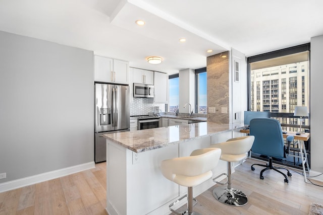 kitchen featuring a breakfast bar area, stainless steel appliances, white cabinetry, light stone countertops, and a peninsula