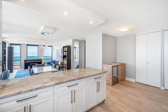 kitchen with light wood finished floors, white cabinets, light stone counters, open floor plan, and pendant lighting