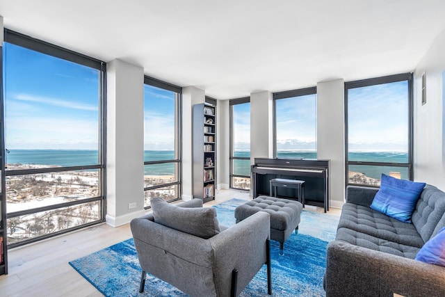 living area with a water view, light wood-type flooring, floor to ceiling windows, and baseboards