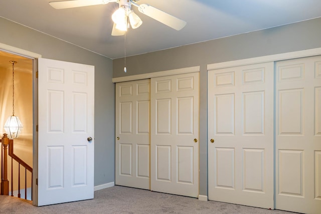 unfurnished bedroom with multiple closets, light colored carpet, and ceiling fan