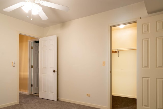 unfurnished bedroom featuring dark carpet, a walk in closet, a closet, and ceiling fan