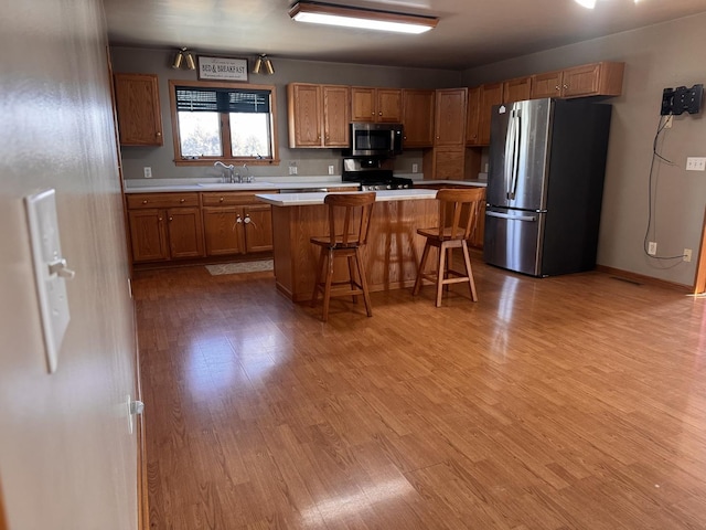 kitchen with a kitchen island, appliances with stainless steel finishes, sink, a kitchen breakfast bar, and light wood-type flooring