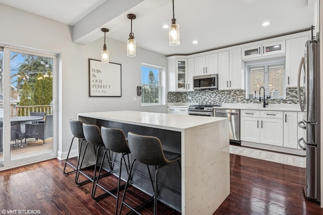 kitchen featuring dark wood finished floors, decorative backsplash, appliances with stainless steel finishes, a breakfast bar, and light countertops