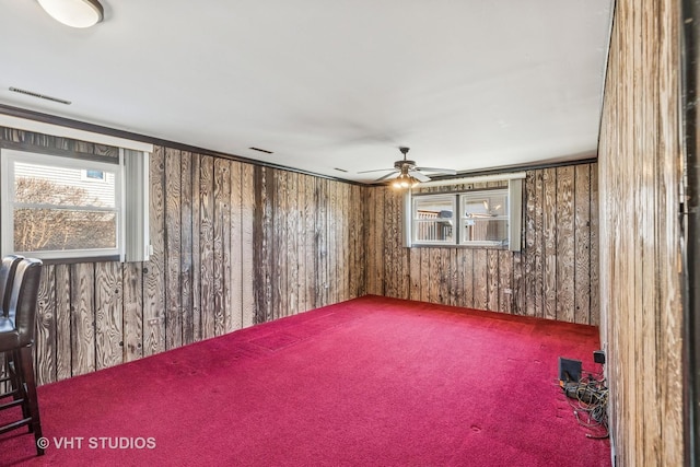 carpeted spare room featuring wood walls, visible vents, and a ceiling fan