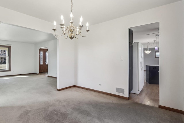 carpeted spare room with an inviting chandelier