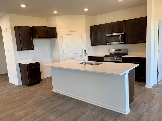 kitchen featuring sink, hardwood / wood-style flooring, stainless steel appliances, dark brown cabinetry, and an island with sink