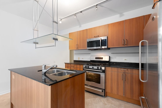 kitchen with rail lighting, sink, appliances with stainless steel finishes, dark stone counters, and a kitchen island with sink