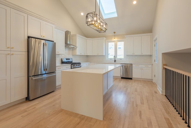 kitchen featuring white cabinetry, stainless steel appliances, a center island, and wall chimney range hood