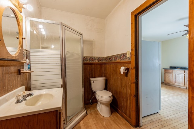 bathroom with toilet, wood-type flooring, vanity, a shower with door, and ceiling fan