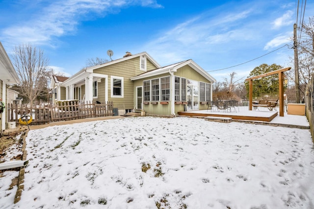 snow covered rear of property featuring a sunroom and a deck