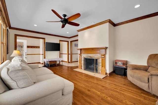 living room with crown molding, ceiling fan, wood-type flooring, and a fireplace