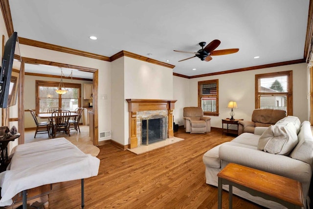 living room with hardwood / wood-style flooring, ceiling fan, ornamental molding, and a fireplace