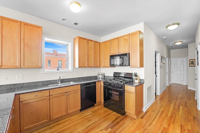 kitchen featuring dark countertops, visible vents, light wood-style flooring, a sink, and black appliances