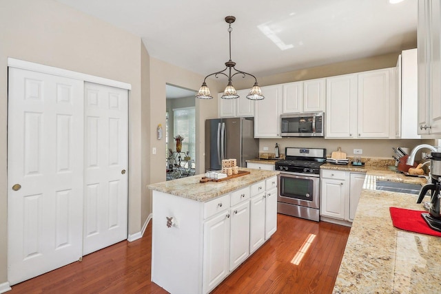 kitchen with a kitchen island, appliances with stainless steel finishes, pendant lighting, and white cabinets