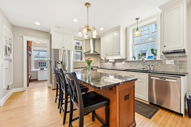 kitchen featuring wall chimney exhaust hood, radiator heating unit, appliances with stainless steel finishes, light wood-style floors, and a sink