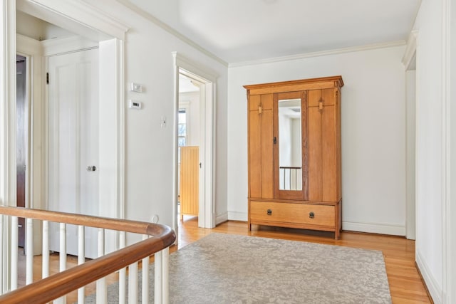 corridor featuring light wood finished floors, baseboards, and ornamental molding