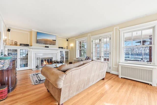 living area with french doors, radiator heating unit, a glass covered fireplace, wood finished floors, and baseboards