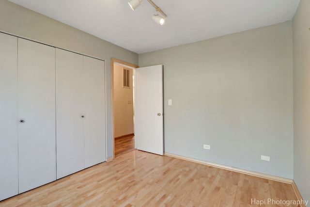 unfurnished bedroom with track lighting, a closet, and light wood-type flooring