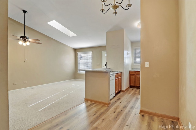 kitchen with sink, ceiling fan, dishwasher, lofted ceiling with skylight, and light wood-type flooring