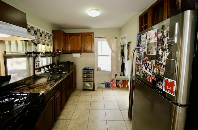 kitchen featuring under cabinet range hood, a sink, black gas stove, freestanding refrigerator, and light tile patterned flooring