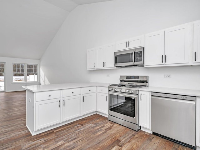 kitchen with lofted ceiling, appliances with stainless steel finishes, kitchen peninsula, and white cabinets