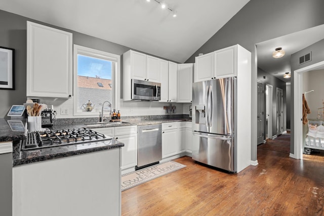 kitchen featuring vaulted ceiling, appliances with stainless steel finishes, hardwood / wood-style floors, white cabinetry, and sink