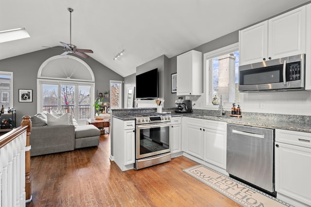 kitchen with dark stone countertops, stainless steel appliances, kitchen peninsula, and white cabinets