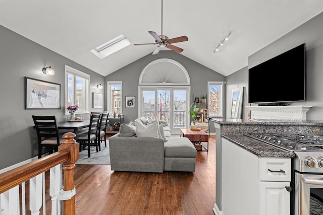 living room featuring dark hardwood / wood-style flooring, lofted ceiling with skylight, and ceiling fan