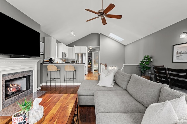 living room with hardwood / wood-style flooring, vaulted ceiling with skylight, and ceiling fan