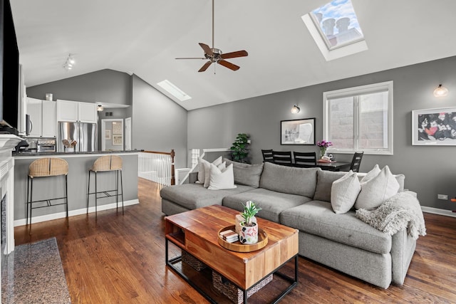 living room featuring ceiling fan, dark wood-type flooring, and vaulted ceiling with skylight