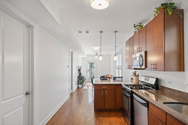 kitchen with appliances with stainless steel finishes, light hardwood / wood-style floors, decorative light fixtures, kitchen peninsula, and dark stone counters