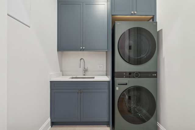 clothes washing area with cabinets, stacked washer / drying machine, and sink