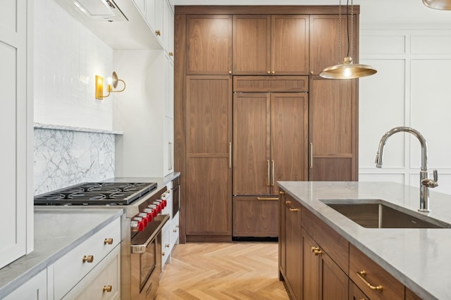 kitchen featuring white cabinetry, sink, light parquet floors, high end appliances, and light stone countertops