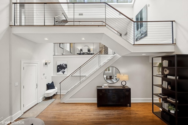 staircase featuring a high ceiling, baseboards, and wood finished floors