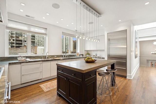 kitchen with built in fridge, a breakfast bar area, butcher block counters, white cabinets, and wood finished floors