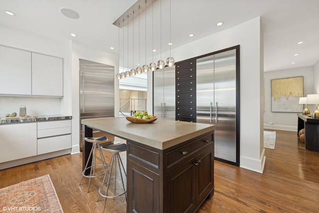 kitchen with a breakfast bar area, dark brown cabinetry, recessed lighting, dark wood-style flooring, and high end fridge