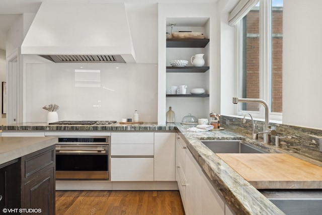 kitchen featuring appliances with stainless steel finishes, white cabinetry, a sink, wood finished floors, and premium range hood